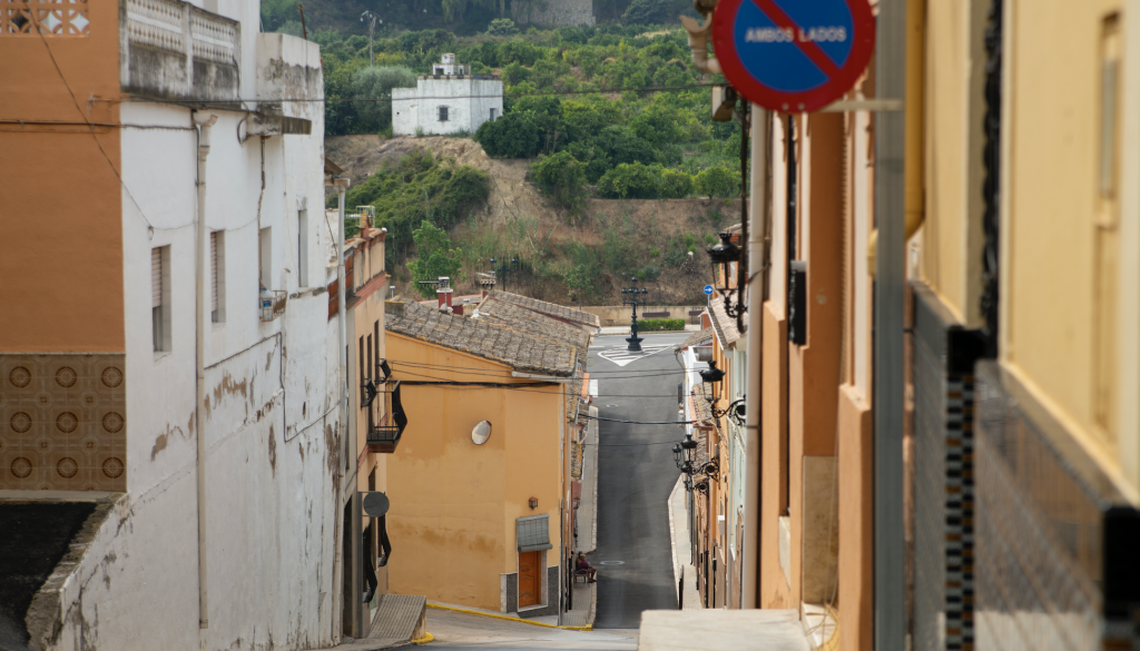 El carrer Major descendeix fins a arribar a l'exterior del poble. Al fons dalt, una casa blanca mitjana envoltada de fruiteres.