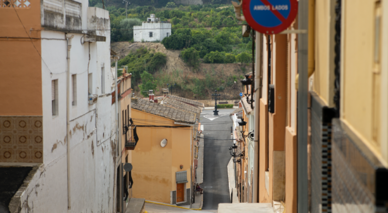 El carrer Major descendeix fins a arribar a l'exterior del poble. Al fons dalt, una casa blanca mitjana envoltada de fruiteres.