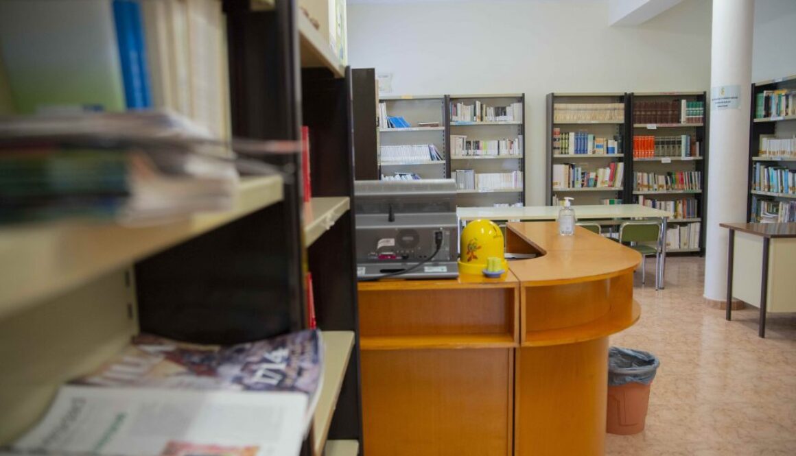 Sala de lectura de la biblioteca municipal amb taulell i prestatgeries per a llibres i revistes.