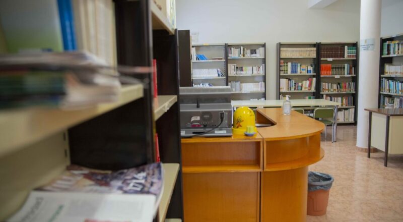 Sala de lectura de la biblioteca municipal amb taulell i prestatgeries per a llibres i revistes.