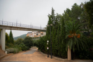 Part del parc Jaume I amb un camí de terra, arbratge i dalt, una passarel·la que travessa el parc.